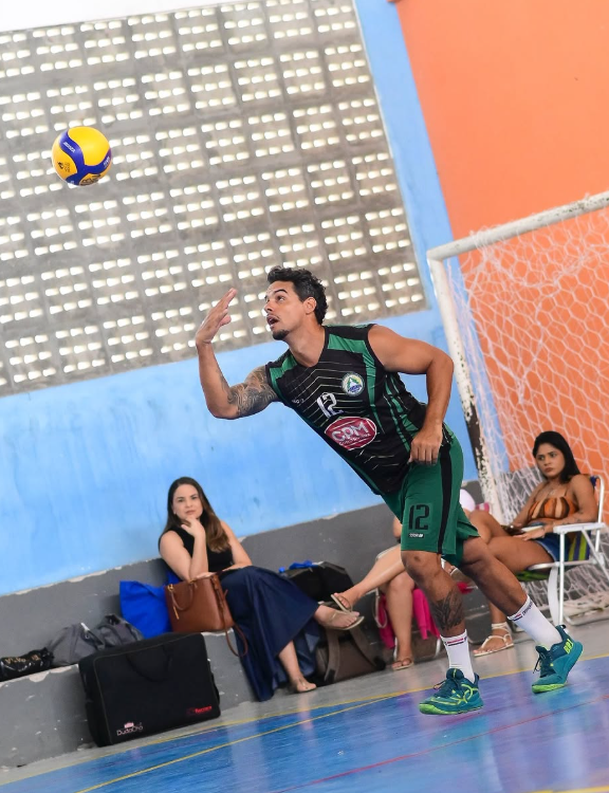 Bruno sacando em quadra com uniforme escuro e verde