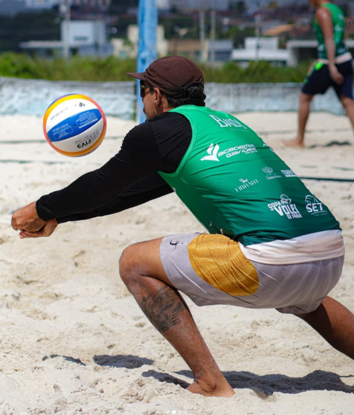 Bruno de verde recebendo uma bola na areia, visto de lado